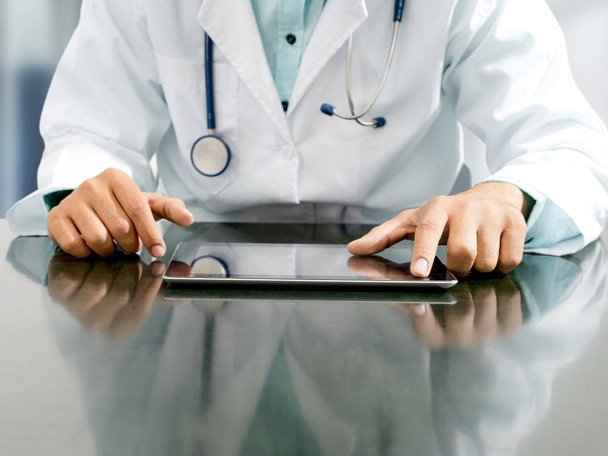 A doctor sitting at a table with a tablet in front of him.